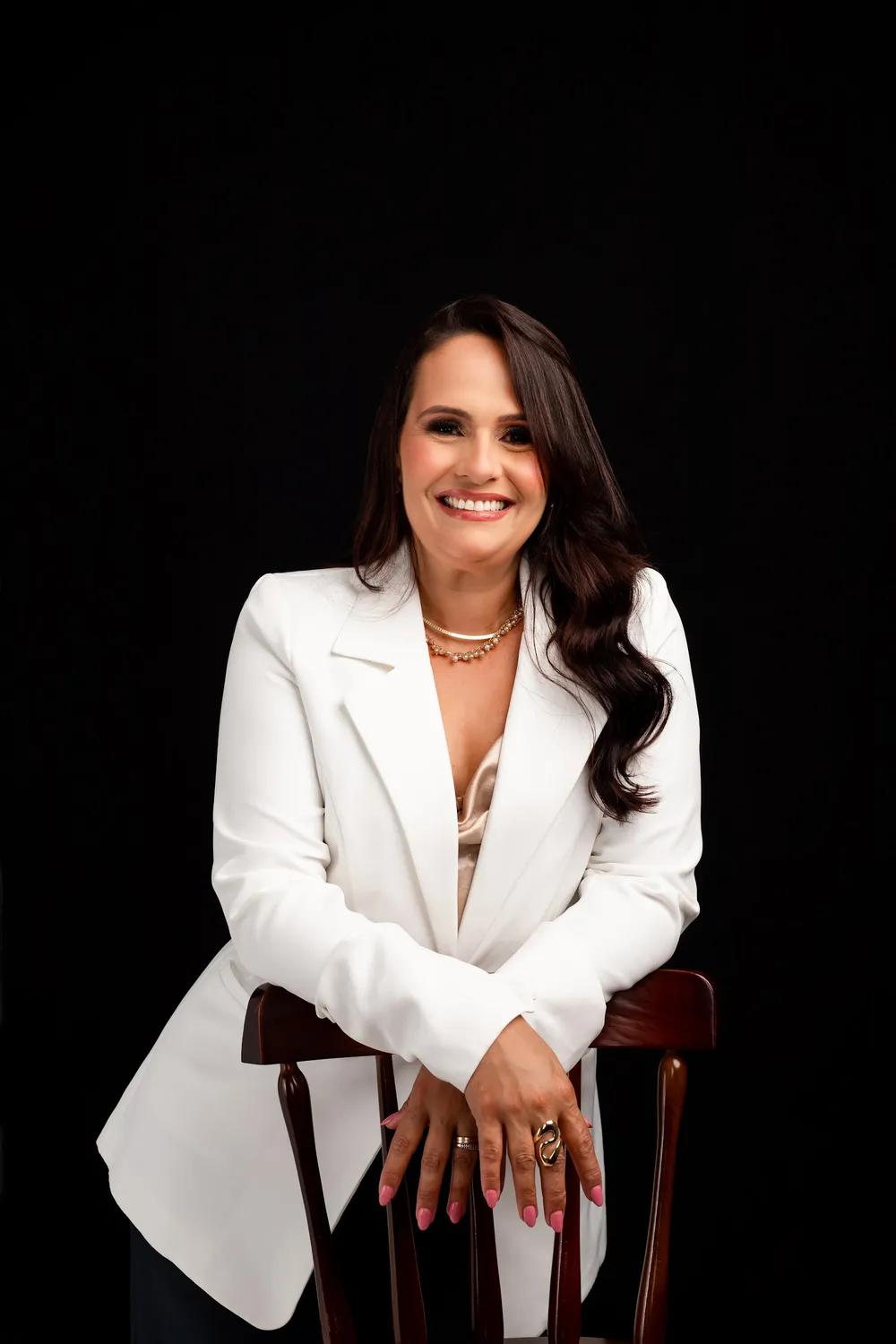 Dra. Danielle Saar, cirurgiã-dentista, de blazer branco em fundo escuro